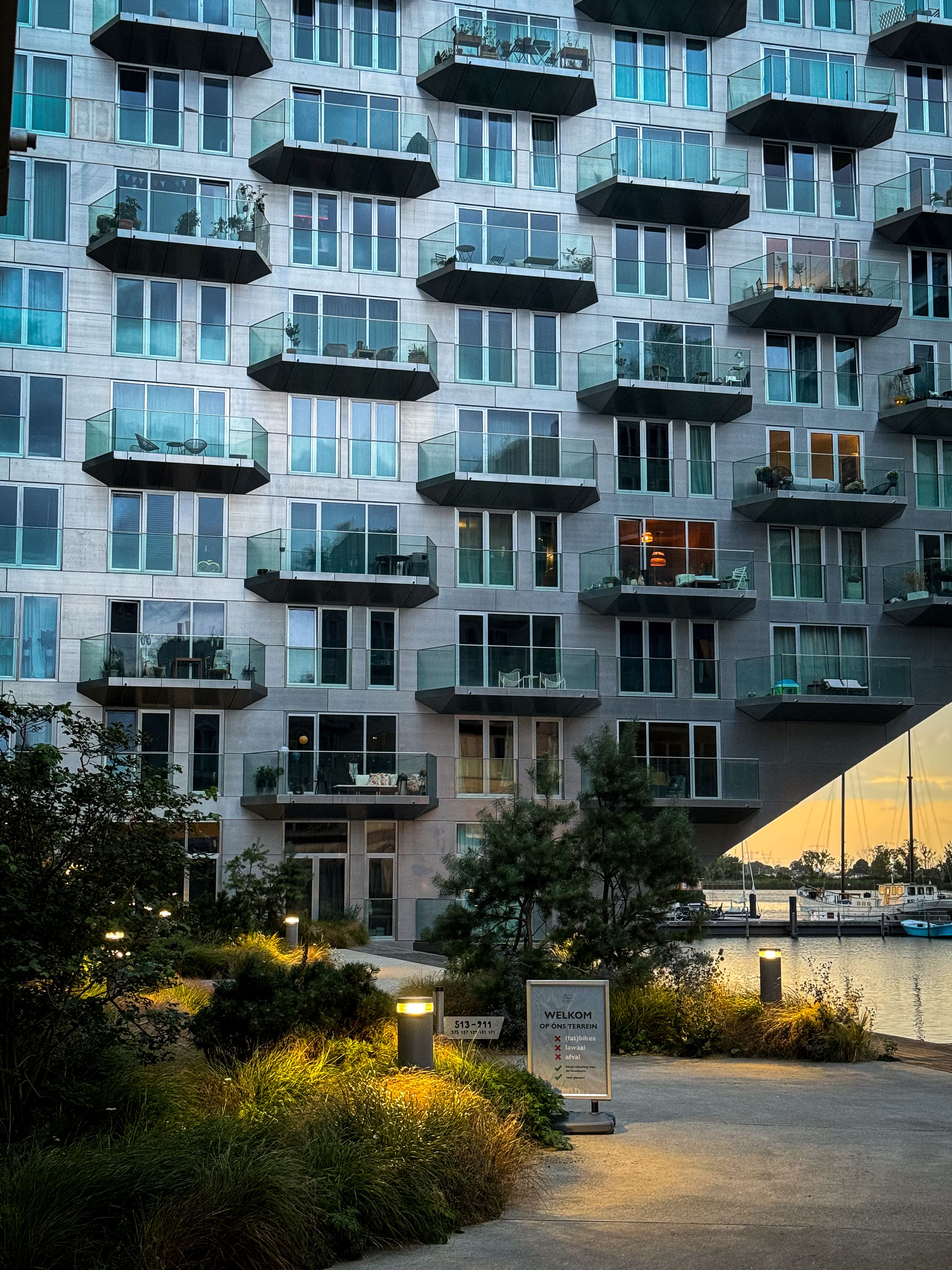 Real Amsterdam residential building at dusk, cantilevered glass balconies and warm interior lights