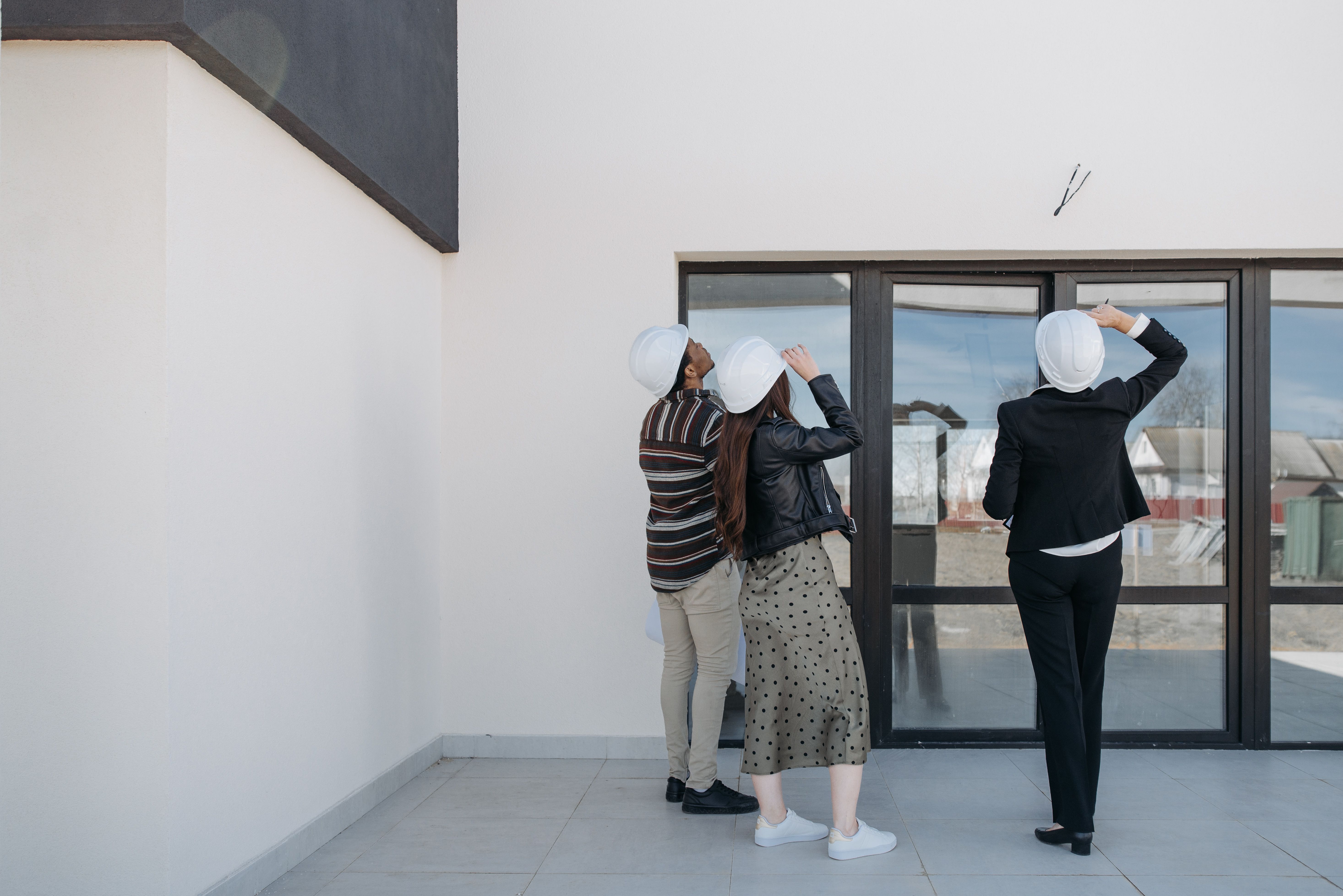 Three professionals in hard hats assessing a real building exterior; people positioned right with generous quiet space on left