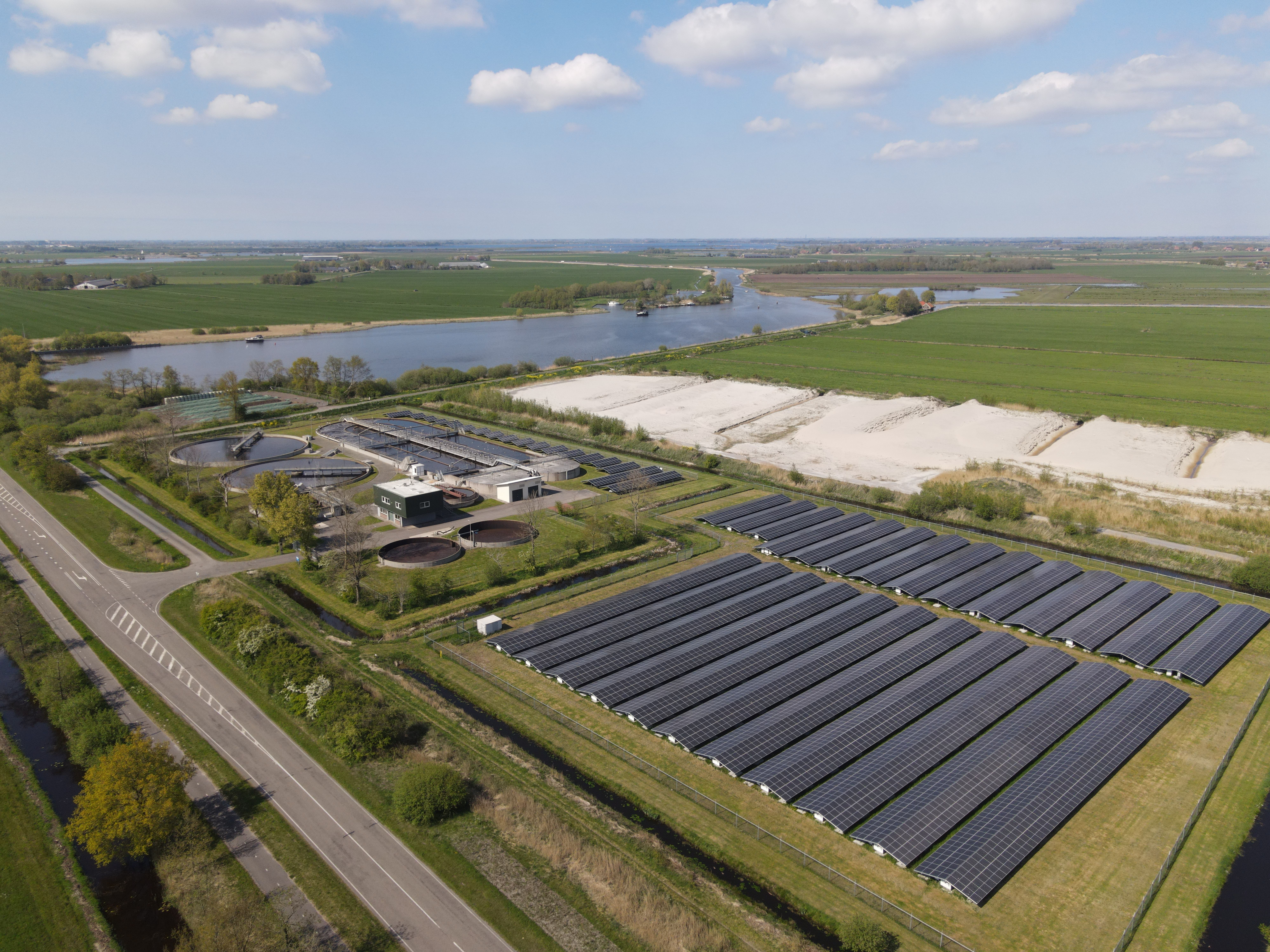 Solar installation amid fields and waterways in Joure, Netherlands; restrained green, steel-blue and charcoal palette